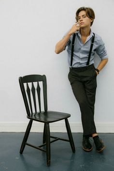 a young man leaning against a wall next to a chair with his hand on his chin