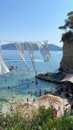 many people are swimming in the water near some rocks and umbrellas with white sheets hanging over them