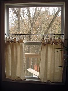 an open window with curtains and a bench in front of the treetops outside it