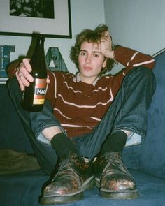 a person sitting on a couch with a beer in their hand and one foot up