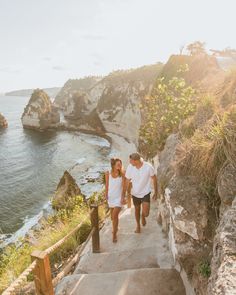 a man and woman walking up some stairs near the ocean