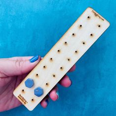 a hand holding a wooden board with holes in it and two blue rocks on top