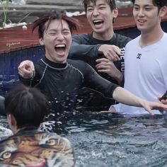 three young men are playing in the water with an adult tiger and another man who is wearing a wet suit