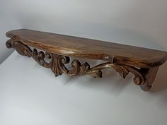 an ornate wooden shelf with carved designs on it's sides, against a white wall