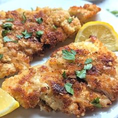 two pieces of fried chicken on a white plate with lemon wedges and parsley