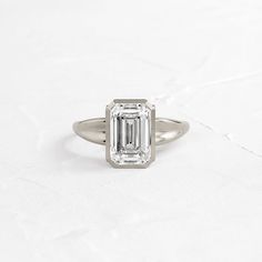 The Fluctuate Ring combines drama with intrigue. An emerald cut diamond of your choice is set in a delicate bezel along a dramatically bubbled and tapered sweetheart band of 14k gold or platinum. Our expertise in metalwork means that both the slender bezel and thick band are sculpted with precision, creating complementary contrast. The bezel setting is raised by single prongs which provide more than merely elevation. Each prong is accented by three round cut diamonds that grow in size as they approach the crown of the focal stone. Between two sets of prongs rests another hidden diamond, causing the ring to appear to be held up by nothing other than a cradle of diamonds. Through duality, the Fluctuate Ring brings balance to a changing tide. Ring Emerald Cut, Emerald Cut Diamond, Ring Emerald, Emerald Cut Diamonds, Round Cut Diamond, Bezel Setting, Emerald Cut, Metal Working, Round Cut