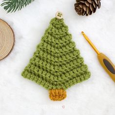 a crocheted christmas tree ornament next to a pine cone and knitting needles