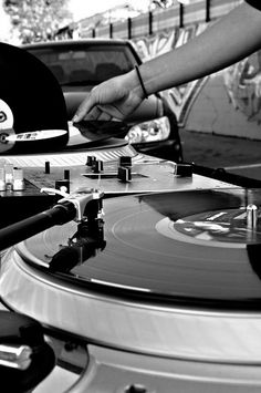 a record player is playing music in front of some parked cars with his hand on the turntable