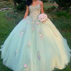 a woman in a green and pink ball gown standing on the grass with her bouquet