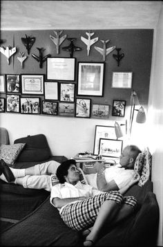 black and white photograph of two men laying on a couch in front of a wall with pictures