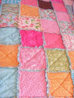 a quilted blanket with different colors and patterns on it, sitting on top of a bed