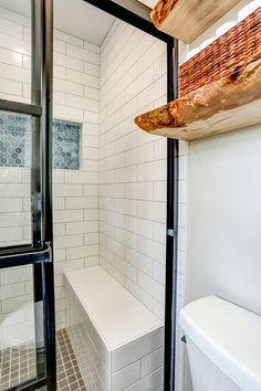 Master bathroom remodel includes glass shower doors with matte-black grids, enclosing an all-tile shower that features a bench seat and Caribbean-blue tiled niche, swarm gray vanity with white marble top, distressed vinyl plank floor, and floating live-edge wood shelving