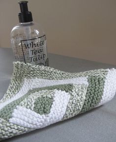 a green and white knitted object next to a bottle of soap on a table