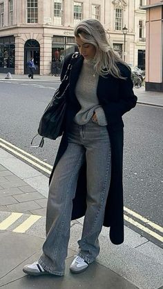 a woman is standing on the sidewalk with her hand in her pocket and looking down