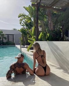 a man and woman sitting on the edge of a swimming pool next to each other