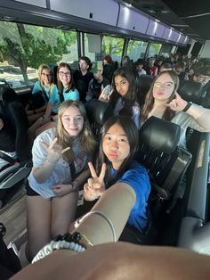 a group of young women sitting in the back of a bus giving thumbs up signs