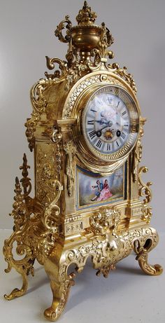 an ornate gold clock with paintings on the front and sides, sitting on a white surface