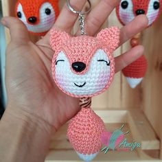 a hand holding three small crocheted keychains in the shape of foxes