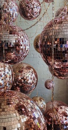 many shiny disco balls hanging from chains in front of a brick wall