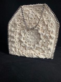 a white crocheted purse with chains hanging from it's sides on a black background