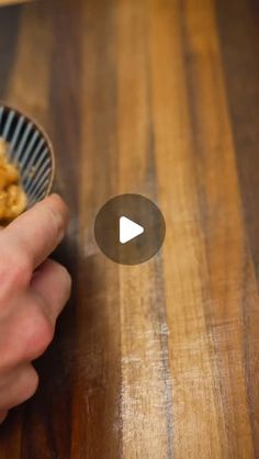 a person holding a bowl filled with food on top of a wooden table next to a knife