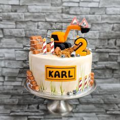 a cake decorated with construction equipment on top of a metal stand in front of a brick wall