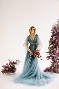 a woman in a blue dress standing next to purple and pink flowers on a white background