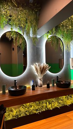 a bathroom with two sinks, mirrors and plants on the wall above them is lit by lights