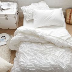 a bed with white sheets and pillows in a room next to a suitcase on the floor