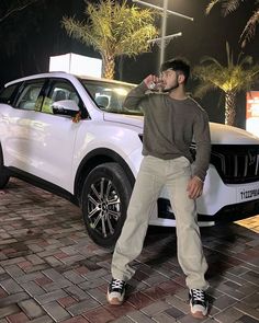 a man standing next to a white car drinking water