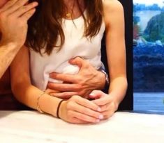 a man and woman sitting next to each other at a table with their hands on the stomach