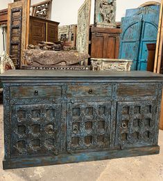 an old wooden cabinet with ornate carvings on the front and sides, surrounded by other antique furniture