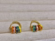 Brighten up your jewelry collection with these playful gold-plated hoop earrings. Each earring features a stack of vibrant enamel rings in a rainbow of colors--orange, pink, teal, and yellow--accented with delicate gold beading for an extra touch of charm. The bold, multicolored design adds a fun, lively element, making these earrings perfect for those who love to make a statement. Lightweight and versatile, they are ideal for adding a pop of color to any casual or festive outfit. These hoops are sure to be your new favorite accessory! Multicolor Huggie Earrings For Gift, Multicolor Huggie Hoop Earrings For Gift, Multicolor Huggie Earrings As Gift, Multicolor Huggie Earrings For Gifting, Multicolor Round Huggie Earrings For Gifts, Multicolor Huggie Hoop Earrings, Multicolor Round Huggie Earrings As Gift, Multicolor Huggie Earrings For Pierced Ears As A Gift, Colorful Trendy Hoop Earrings For Gift