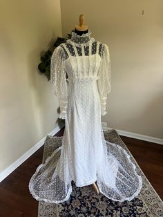 a white dress with sheer neckline and sleeves on display in front of a rug