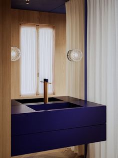 a blue sink in front of a window with curtains on the windowsill and two lights above it