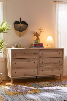 a wooden dresser sitting in front of a window next to a lamp and potted plant