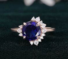 an oval blue sapphire and diamond ring on a black velvet surface with white flowers in the background