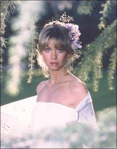 a woman wearing a white dress and flowers in her hair is posing for the camera