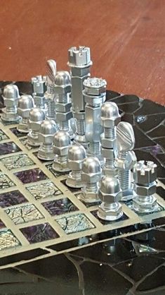 a metal chess set sitting on top of a black marble table next to a wooden floor