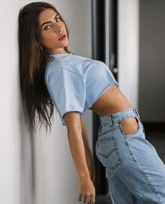 a woman leaning against a wall with her hands on the back of her pants and looking off to the side