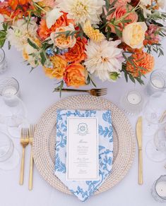 the table is set with blue and white plates, silverware, and orange flowers