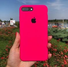 a person holding up a pink iphone case in front of some red flowers and water