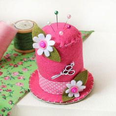 a pink hat with flowers on it sitting next to spools of thread and scissors