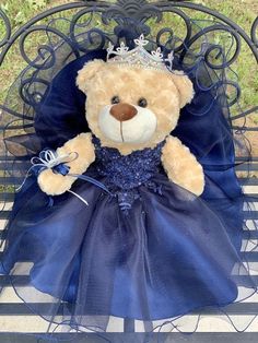 a teddy bear dressed in a blue dress sitting on a bench with a tiara