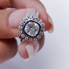 a woman's hand holding a ring with a diamond in the center and surrounded by smaller diamonds