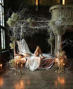 a woman sitting on top of a bed surrounded by candles and trees in front of a window