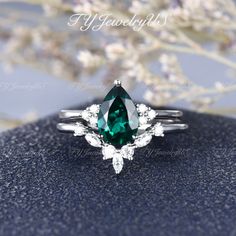 a green and white diamond ring sitting on top of a blue stone surface with flowers in the background