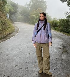 a woman standing in the middle of a road on a foggy day with trees and bushes behind her