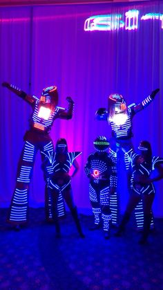 three people dressed in black and white costumes are dancing with their arms outstretched while wearing bright lights