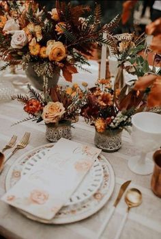 the table is set with orange flowers and white plates, silverware, and candlesticks